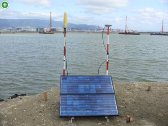 基地局を設置する場所は電波を遮る高い建物などない上空が開けた場所に設置します。電源はバッテリーとソーラーパネルから供給して駆動させています。向かって右が衛星からの情報を受信するGPSアンテナで、左が受信したデータを移動局に送る無線送信機です。